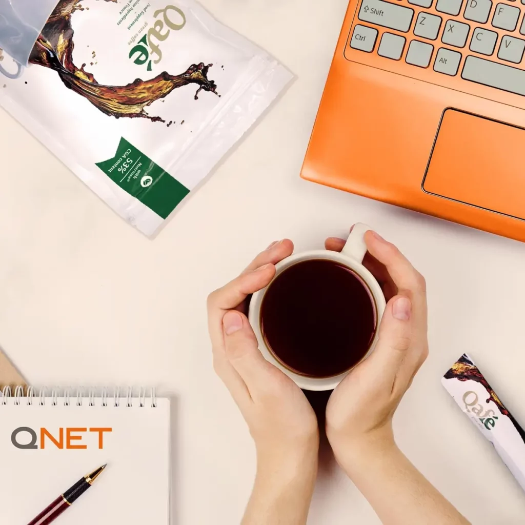 holding a cup of QAFE coffee next to laptop