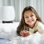 A cheerful young girl happily rests on her bed, with a HomePure air purifier nearby ensuring clean and fresh room air.