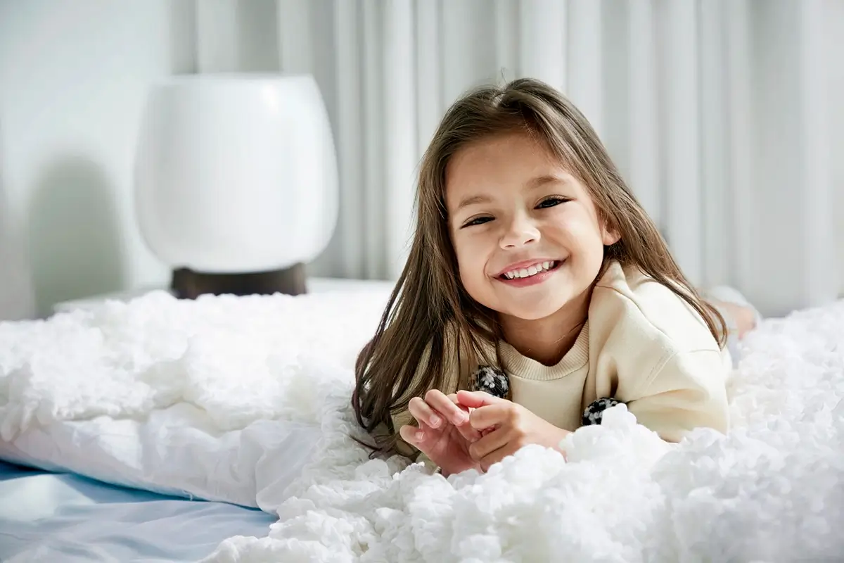 A cheerful young girl happily rests on her bed, with a HomePure air purifier nearby ensuring clean and fresh room air.