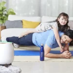 A father doing push-ups with his delighted daughter on his back in the living room, featuring HomePure bottle and HomePure for cleanliness.