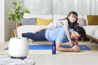 A father doing push-ups with his delighted daughter on his back in the living room, featuring HomePure bottle and HomePure for cleanliness.