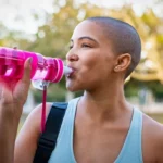 Girl hydrating in the garden post-workout, while another girl beams with happiness