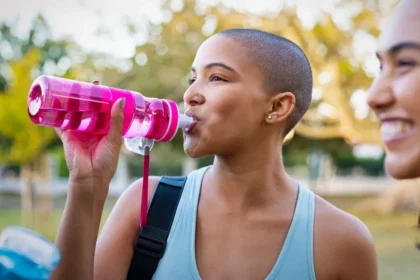 Girl hydrating in the garden post-workout, while another girl beams with happiness