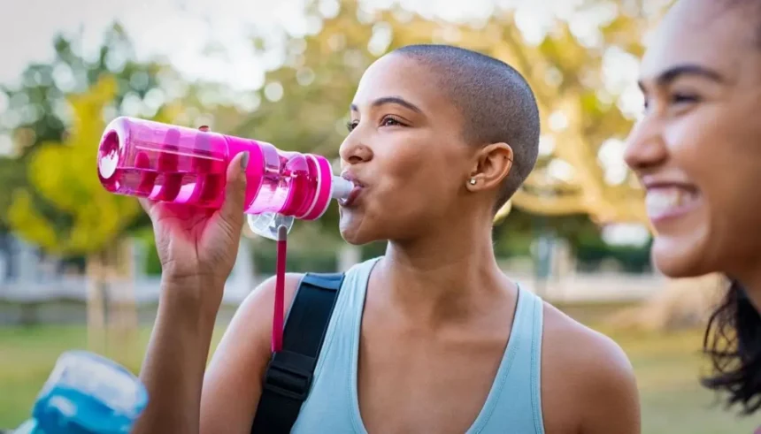 Girl hydrating in the garden post-workout, while another girl beams with happiness