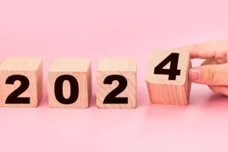 Hand placing a block with the number 4 beside a line of blocks with the numbers 2, 0, 2, symbolizing the change from 2023 to the new year 2024
