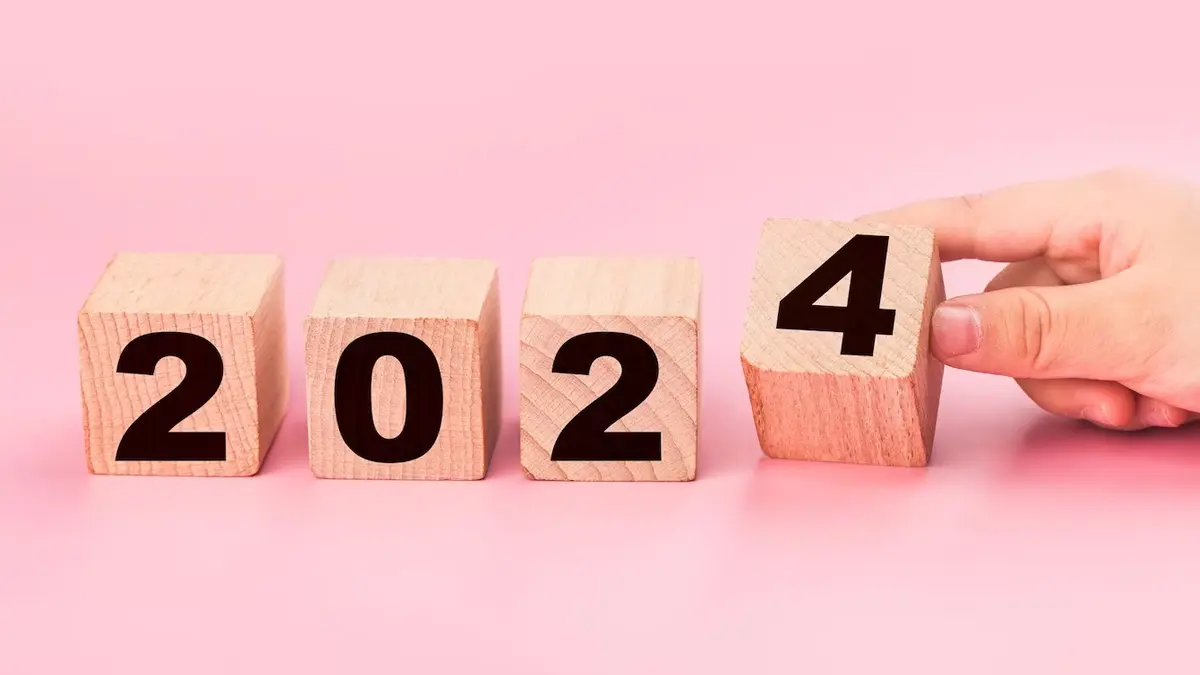 Hand placing a block with the number 4 beside a line of blocks with the numbers 2, 0, 2, symbolizing the change from 2023 to the new year 2024
