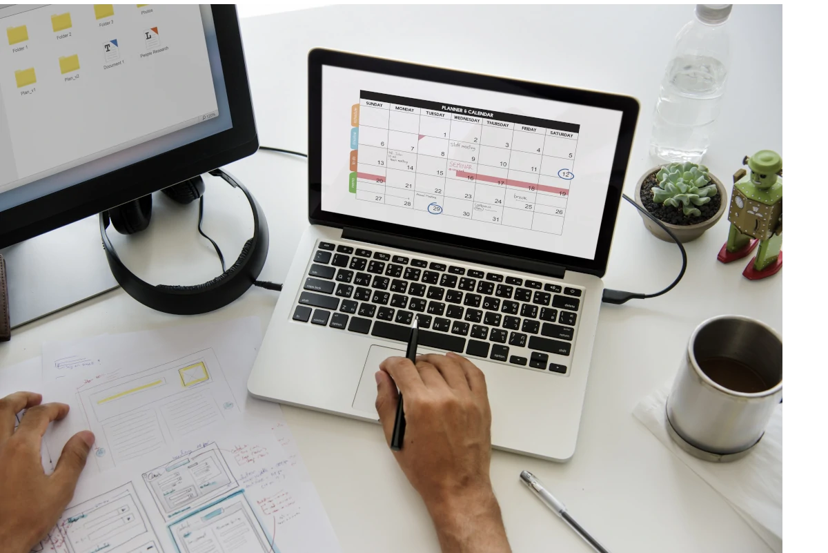 Man working on desk with calendar on laptop and monitor