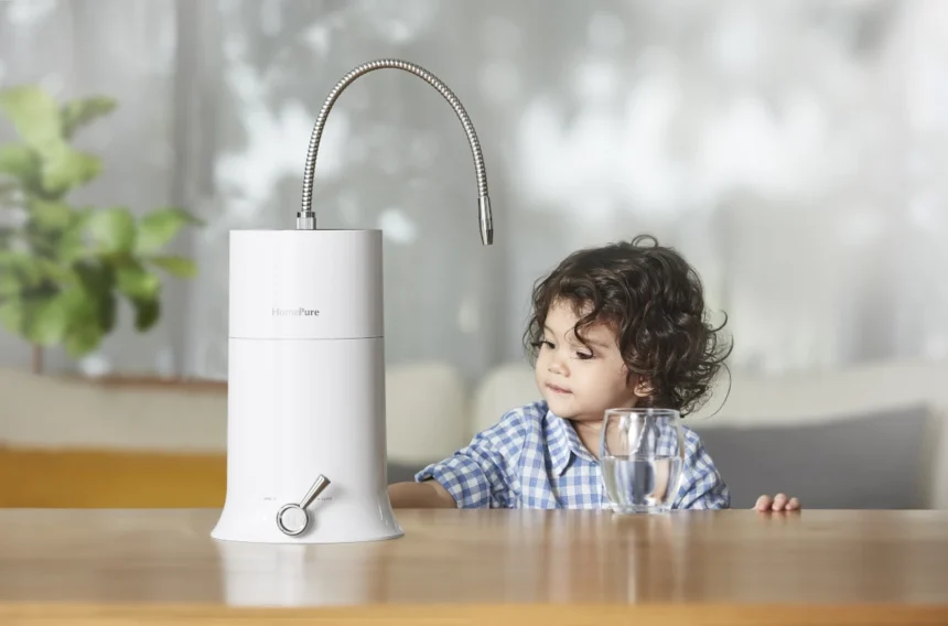 A young boy beside a kitchen counter, with a glass of water nearby, and a HomePure product on the table.