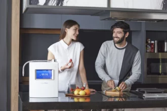 A joyful couple in the kitchen, with a woman ready to enjoy fruit while her husband prepares kiwi with the HomePure Viva Ioniser at the table