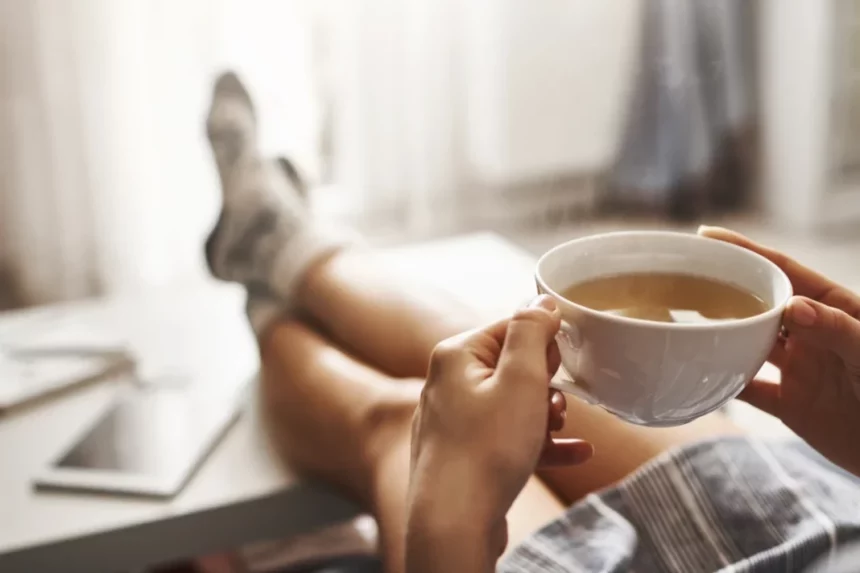 man sitting with legs on table and a cup of coffee in hand