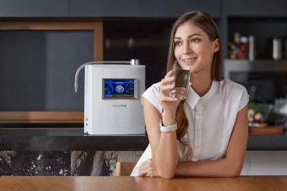 A smiling woman at her kitchen table, holding a glass of HomePure Viva alkaline water, confidently satisfied with her healthy choice.