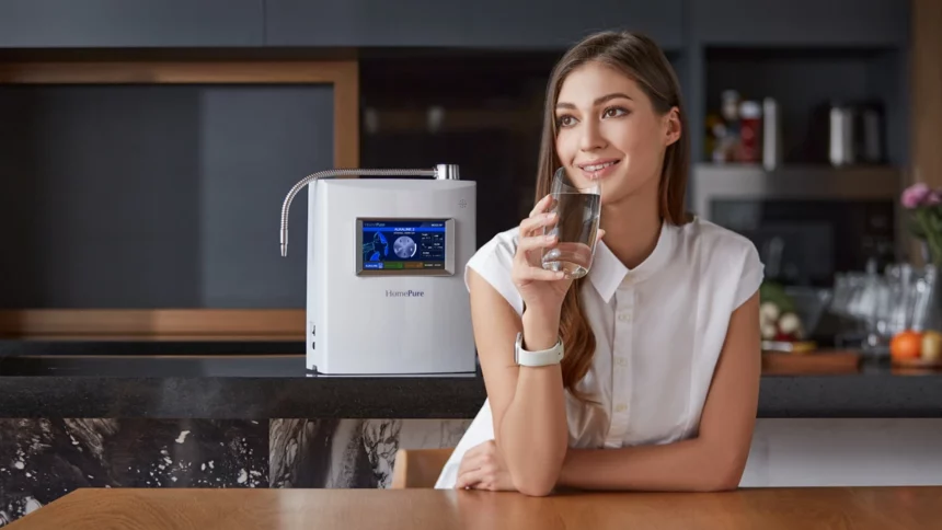 A smiling woman at her kitchen table, holding a glass of HomePure Viva alkaline water, confidently satisfied with her healthy choice.