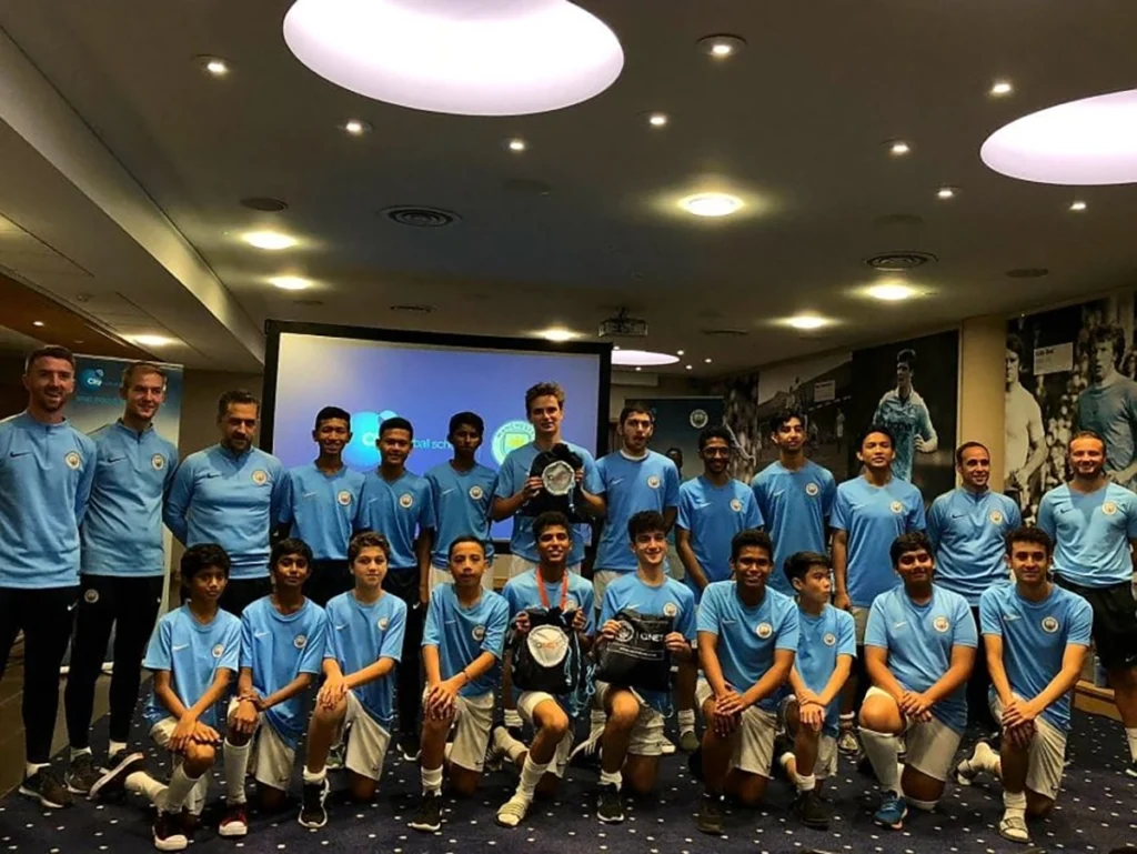 Man City kids posing in Man City etihad campus locker room with man city team. 