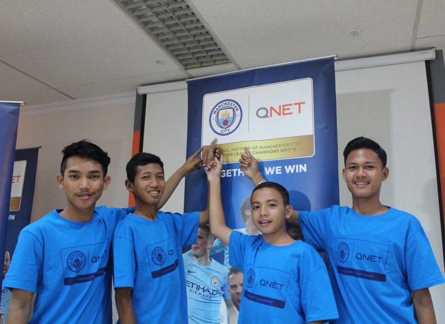 Kids from man city football language school pointing at Manchester city QNET logo smiling