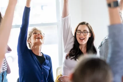 Women of different ages raising their hands in a meeting show why upskilling for women in leadership matter