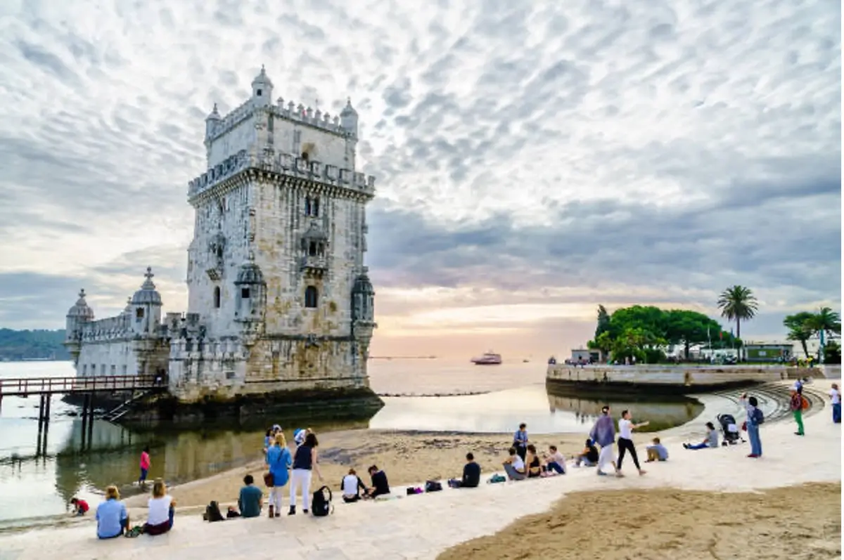 People gathered by the shore in front of an old castle in Lisbon