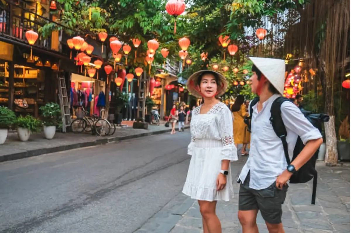 A woman and man wearing non la hats while talking to each other in a Hoi An street