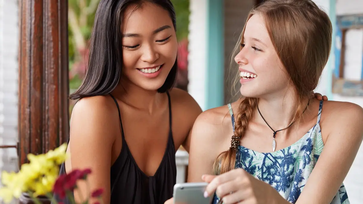 Two women smiling at eachother looking at phone indoors