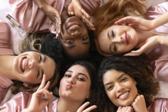 A group of girls dressed in pink, lying in bed with Physio Radiance products and happy smiles