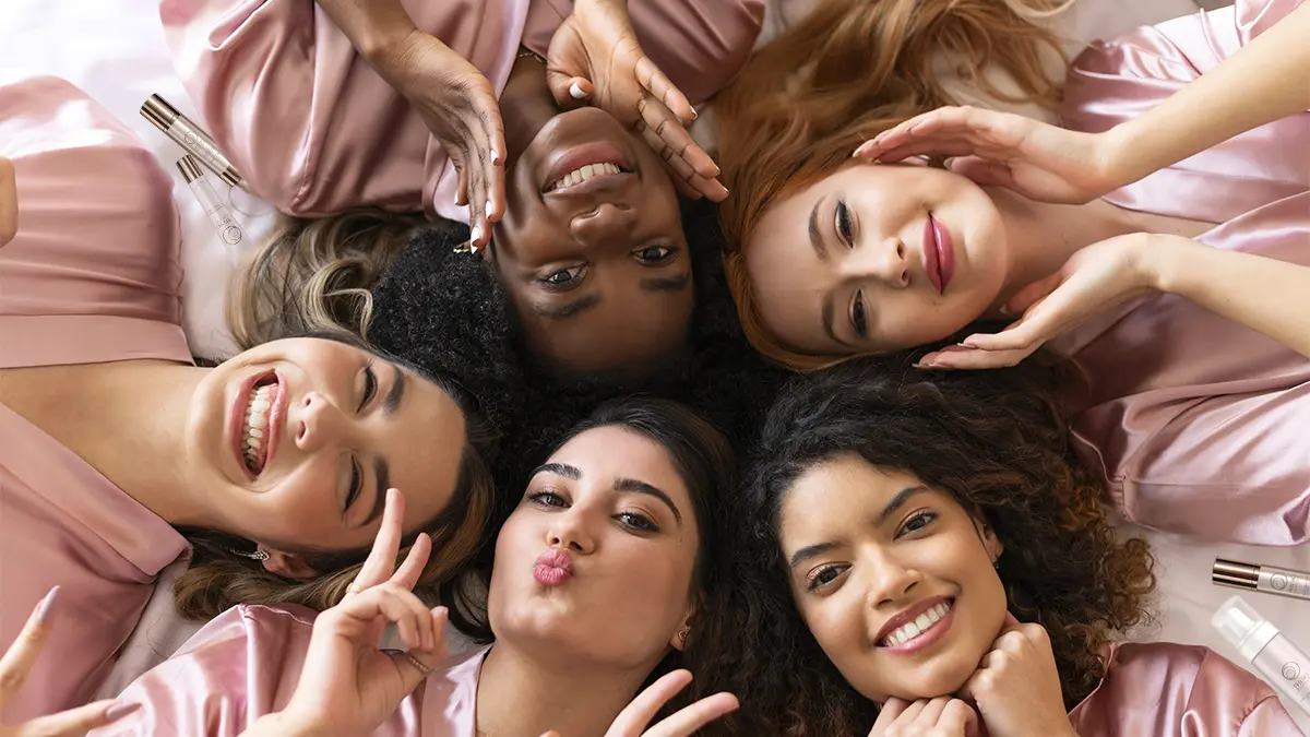 A group of girls dressed in pink, lying in bed with Physio Radiance products and happy smiles