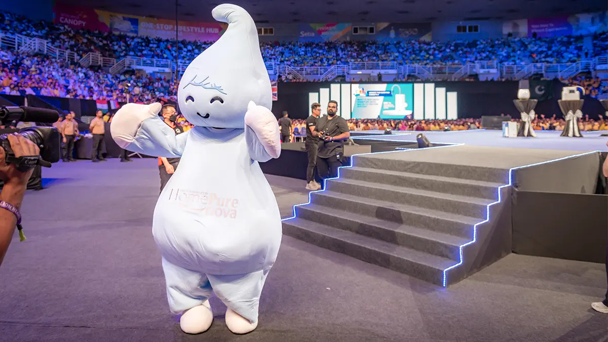 HomePure mascot engaging with attendees in the dynamic V-Convention arena, highlighting QNET's eco-conscious approach to water filtration