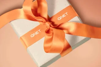 Box with an orange ribbon with QNET branding around it, showing how QNET products are a great way to gift the good life this holiday season