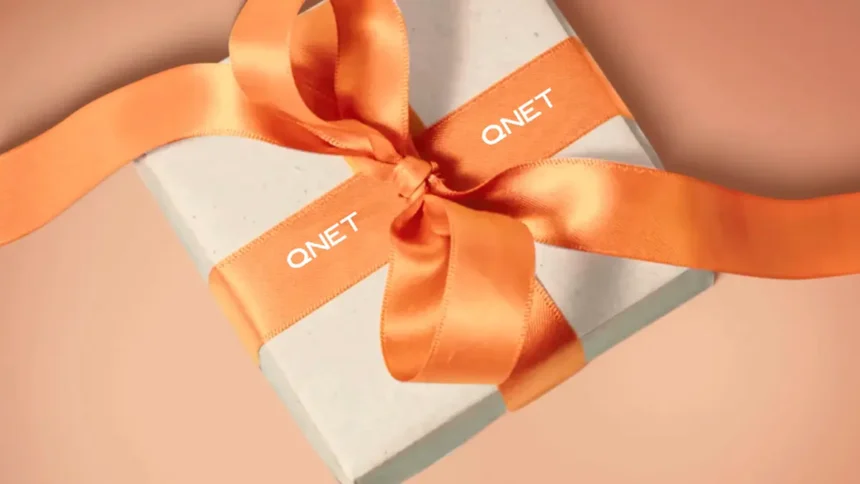 Box with an orange ribbon with QNET branding around it, showing how QNET products are a great way to gift the good life this holiday season