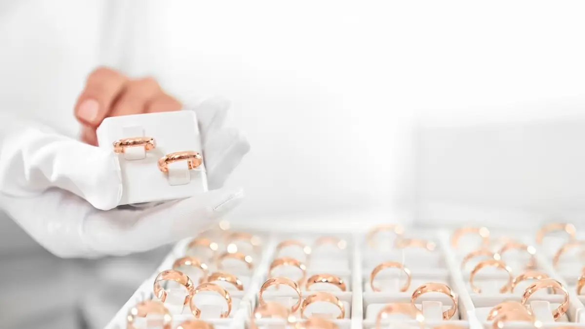 18k gold jewellery rings lined up, with a gloved hand showing a pair from a different angle 