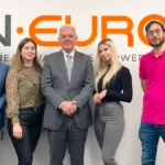 QN Europe Team posing in front of company logo on the wall