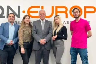 QN Europe Team posing in front of company logo on the wall