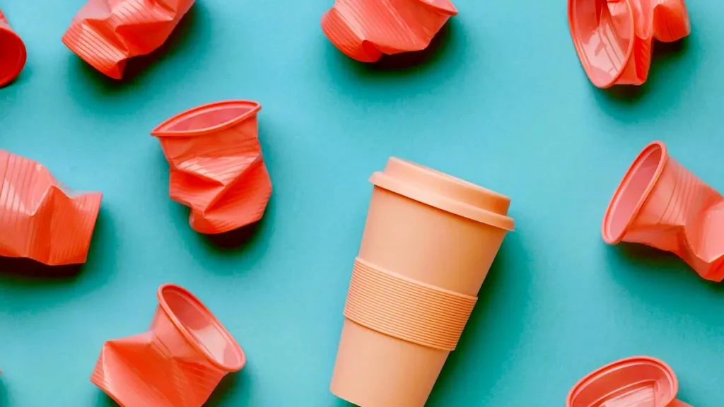 Orange reusable tumbler surrounded by crumpled plastic cups