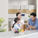 Young couple with a child at the kitchen with muffins, fruit, drinks prepared with the help of HomePure Viva water