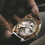 Hand holding a QNET watch with inside mechanism displayed, preparing it for repair