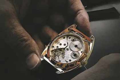 Hand holding a QNET watch with inside mechanism displayed, preparing it for repair