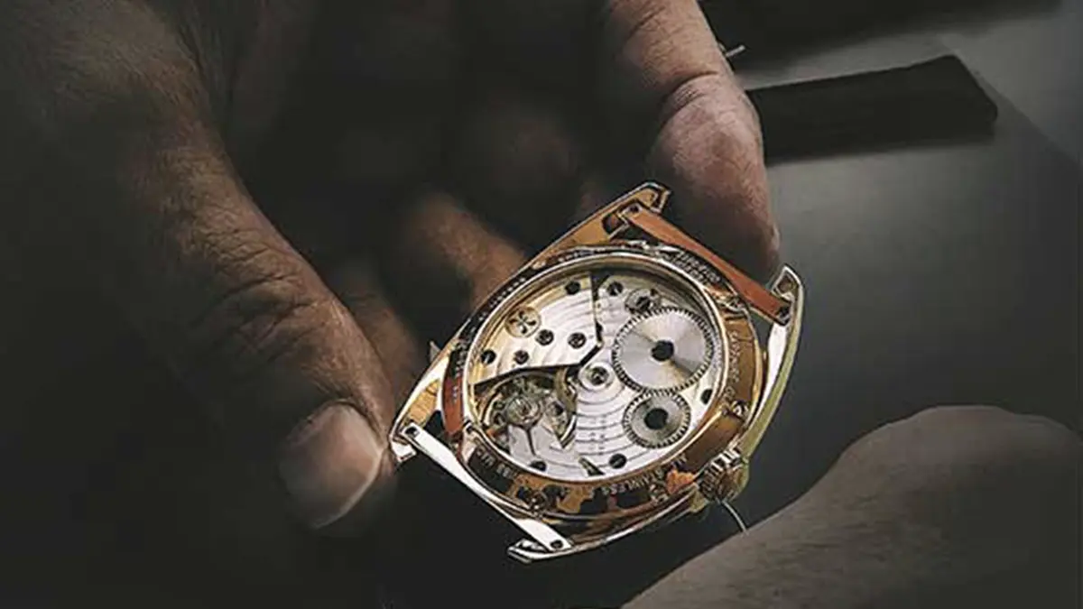 Hand holding a QNET watch with inside mechanism displayed, preparing it for repair