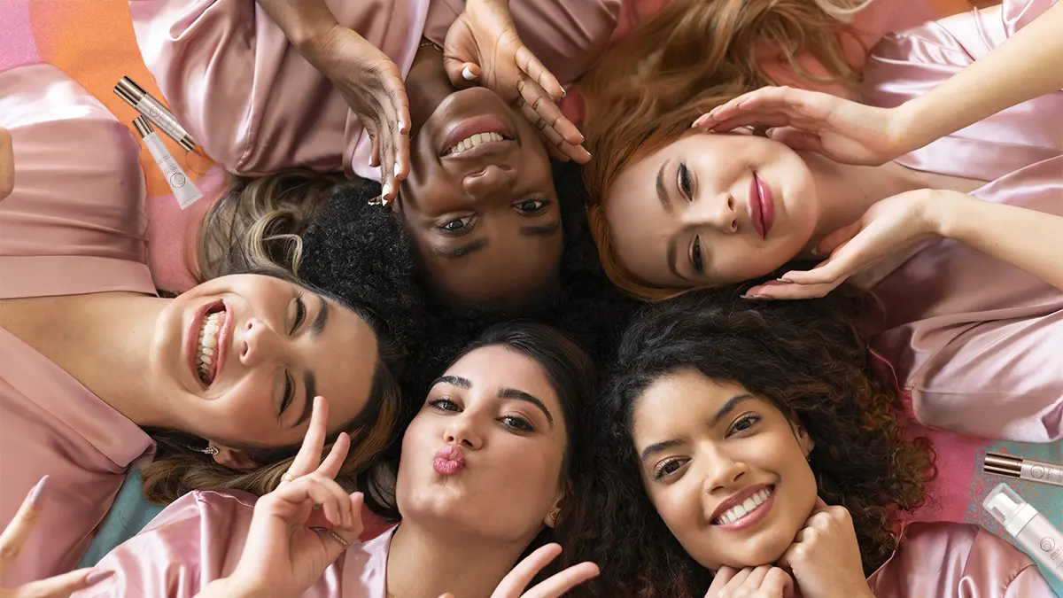 Top view of women at a sleepover smiling for the camera, surrounded by Physio Radiance products