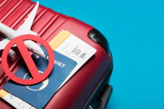 Passport, plane tickets, and a toy plane weighed down by a stop symbol on top of a suitcase, representative of the dangers of travel fraud scams
