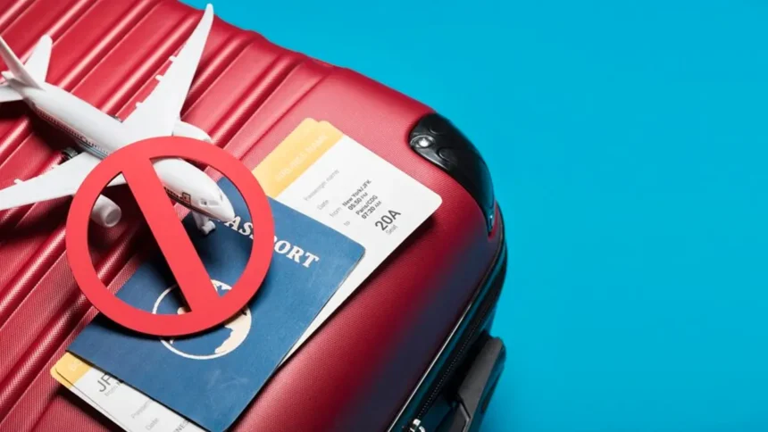 Passport, plane tickets, and a toy plane weighed down by a stop symbol on top of a suitcase, representative of the dangers of travel fraud scams